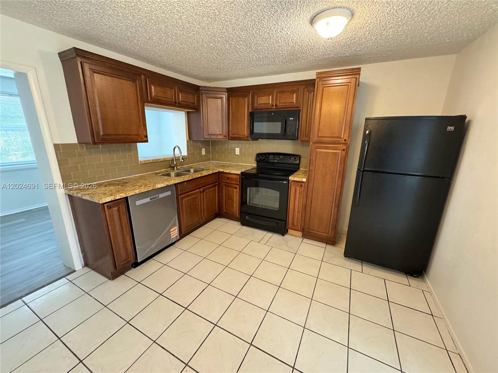 A kitchen features wood cabinets, granite countertops, black appliances, and white tiled flooring — 4361 NW 25th Pl, Lauderhill FL 33313, LAUDERHILL, FL