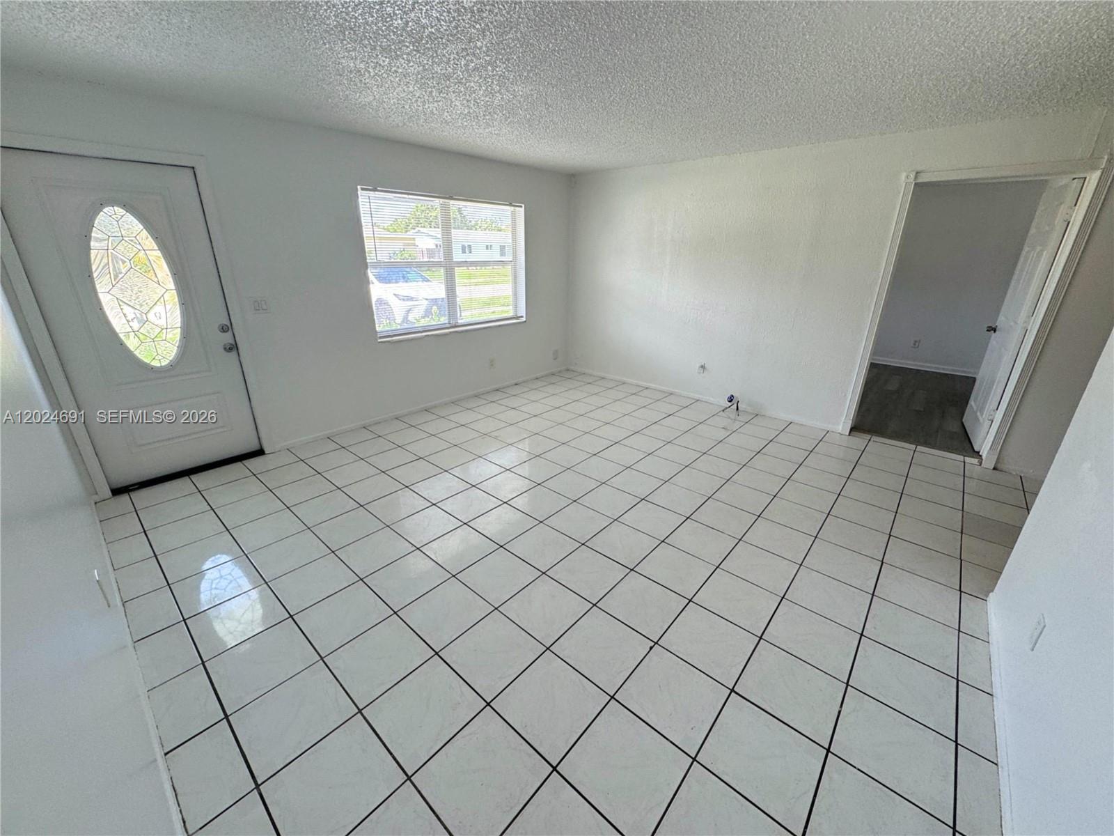 A bright, empty room features white tiled floors, white walls, and a front entry door — 4361 NW 25th Pl, Lauderhill FL 33313, LAUDERHILL, FL