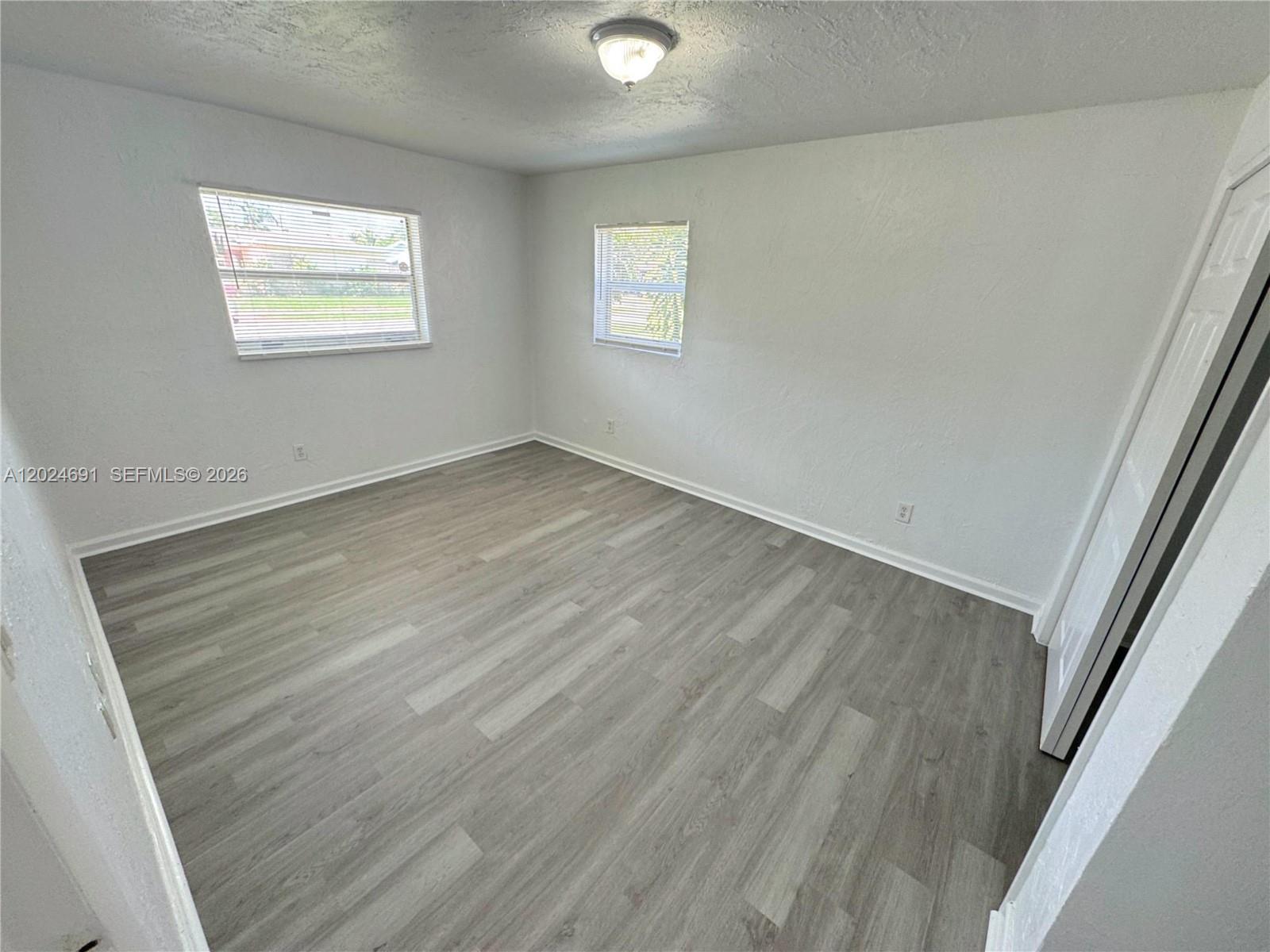An empty bedroom features white walls, light gray wood-look flooring, and two windows — 4361 NW 25th Pl, Lauderhill FL 33313, LAUDERHILL, FL