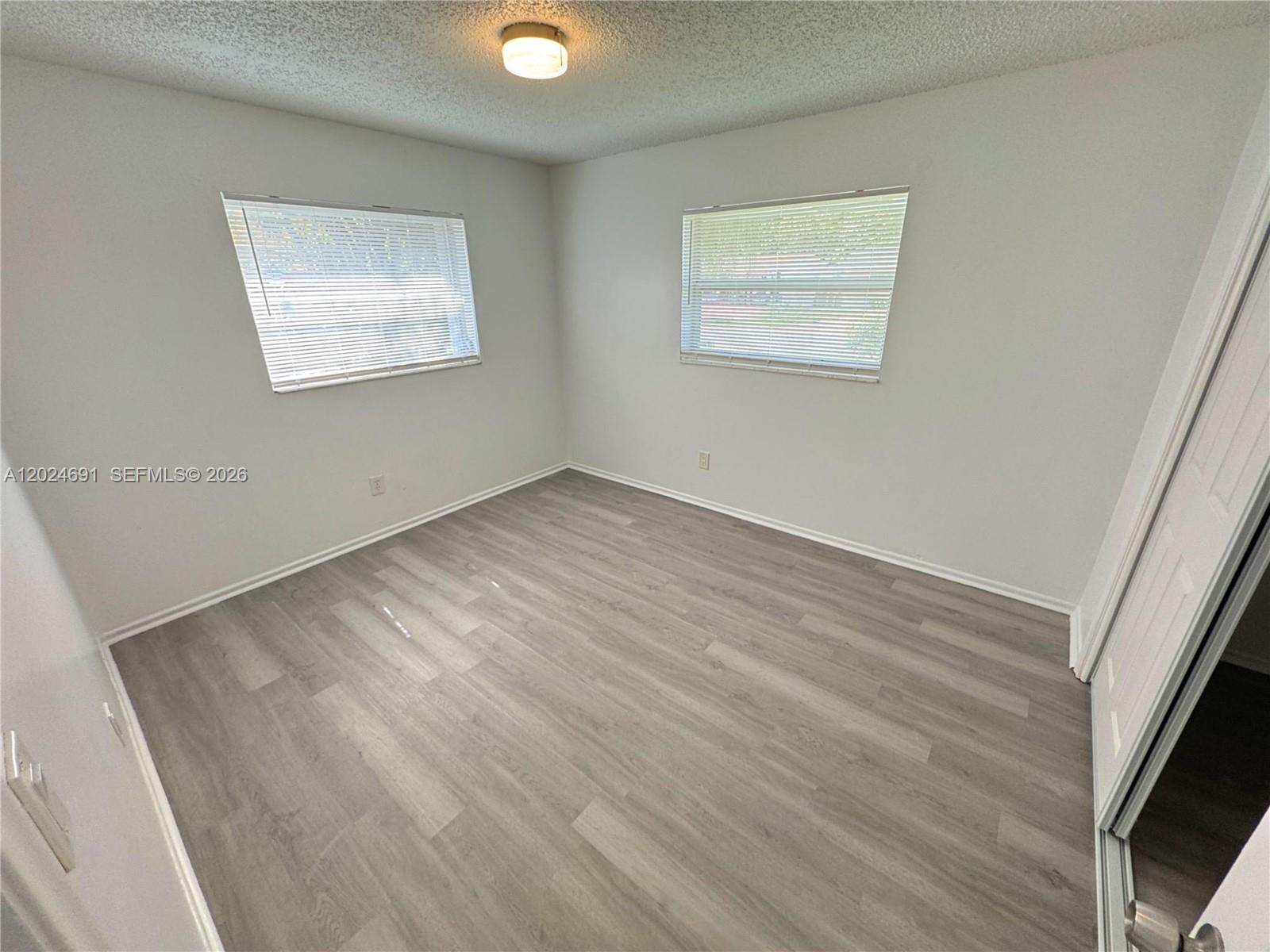 An empty bedroom features light gray walls, wood-look flooring, and two windows with blinds — 4361 NW 25th Pl, Lauderhill FL 33313, LAUDERHILL, FL