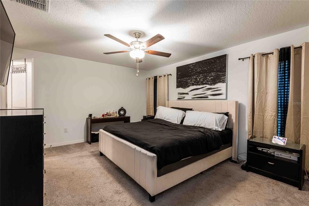 A bedroom features a bed with a light-colored headboard, black bedding, and a ceiling fan — 1658 RED LOOP, LAKELAND, FL