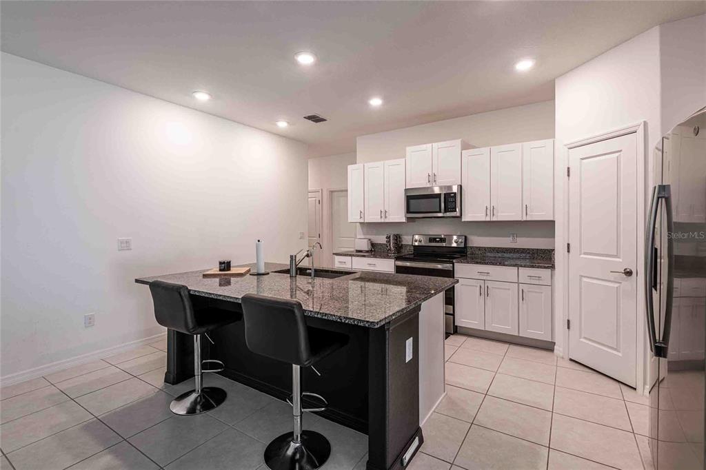 A kitchen features a granite-topped island with bar stools, white cabinetry, and stainless steel appliances — 1658 RED LOOP, LAKELAND, FL