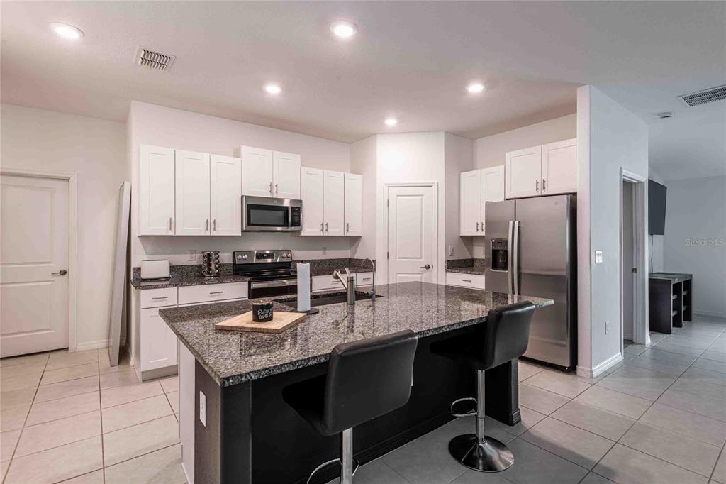 A kitchen features white cabinets, granite countertops, a dark island with seating, and stainless appliances — 1658 RED LOOP, LAKELAND, FL