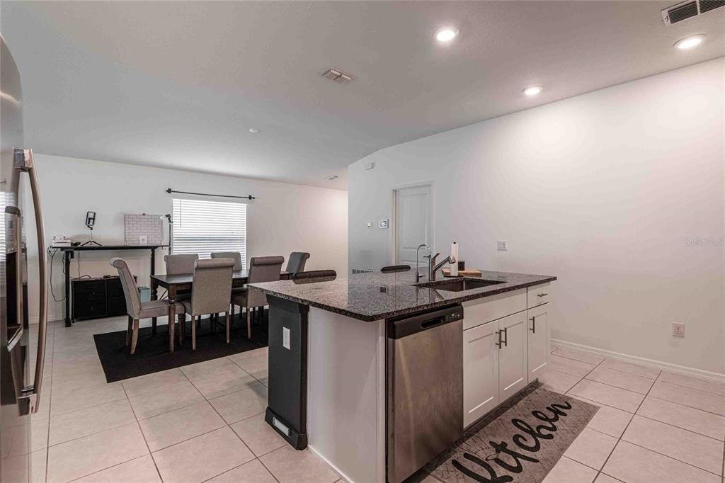 A kitchen island with a granite countertop and stainless steel dishwasher faces a dining area — 1658 RED LOOP, LAKELAND, FL