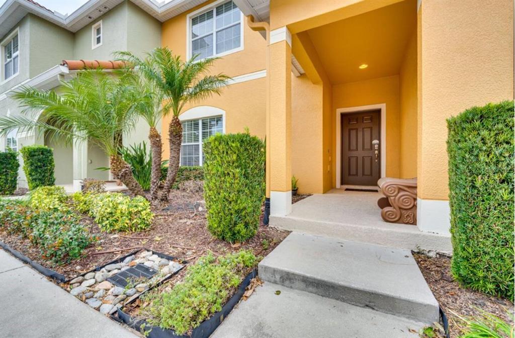 A yellow two-story house exterior features a covered entryway, a brown front door, and landscaping — 8963 CALIFORNIA PALM ROAD, KISSIMMEE, FL