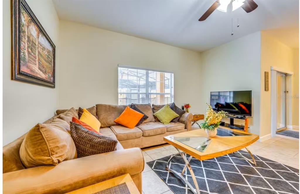 A living room features a tan sectional sofa, a coffee table, and a television — 8963 CALIFORNIA PALM ROAD, KISSIMMEE, FL
