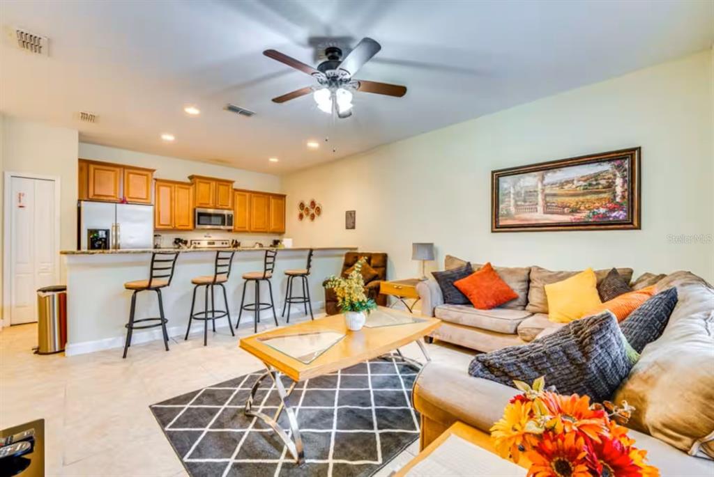 An open-concept living room features a kitchen with bar seating and a beige sofa — 8963 CALIFORNIA PALM ROAD, KISSIMMEE, FL
