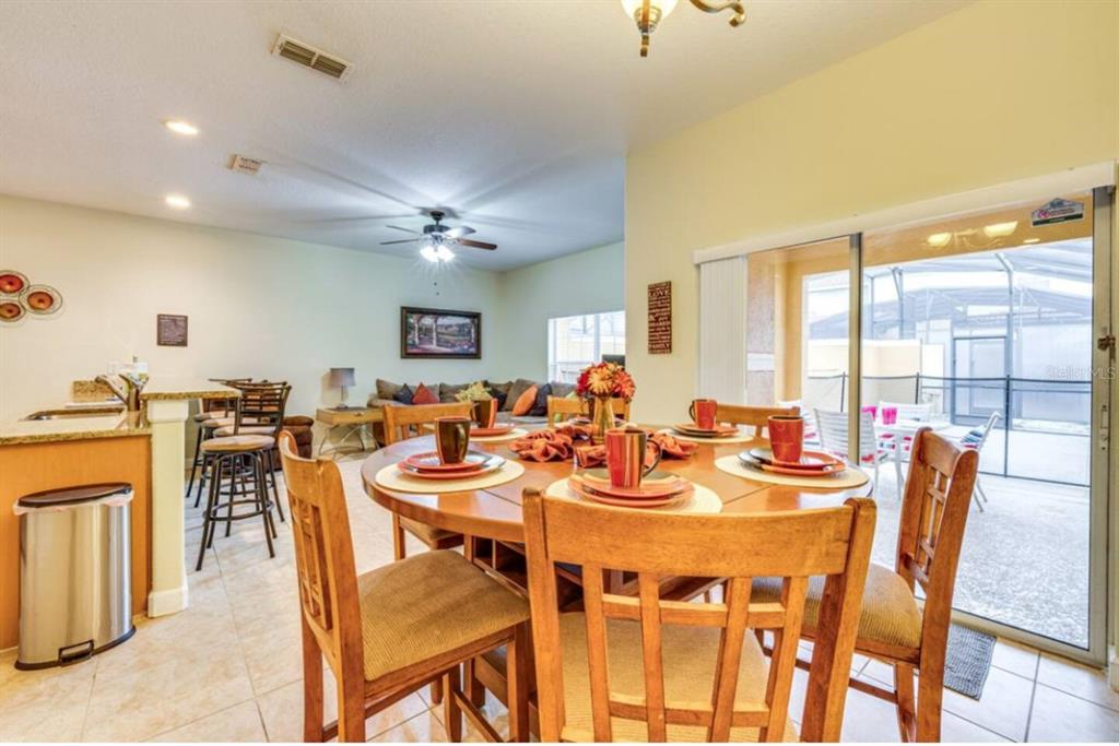 A dining area with a wooden table and chairs sits adjacent to a kitchen and living — 8963 CALIFORNIA PALM ROAD, KISSIMMEE, FL