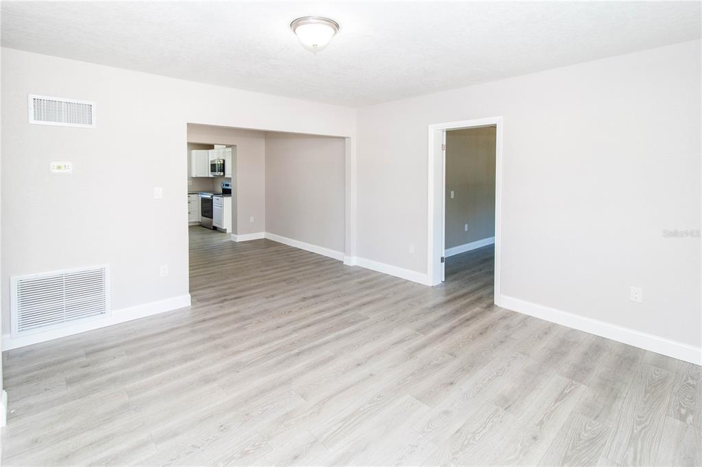 An interior view of a room with light gray walls, wood-look flooring, and a kitchen doorway — 7122 ASTOR DRIVE, NEW PORT RICHEY, FL