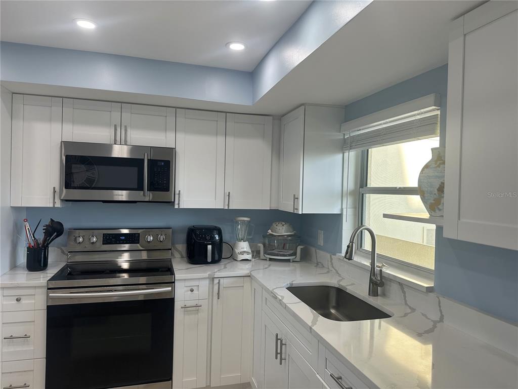 A kitchen with white cabinets, stainless steel appliances, and white quartz countertops with grey veining — 4725 COVE CIRCLE UNIT 804, ST PETERSBURG, FL