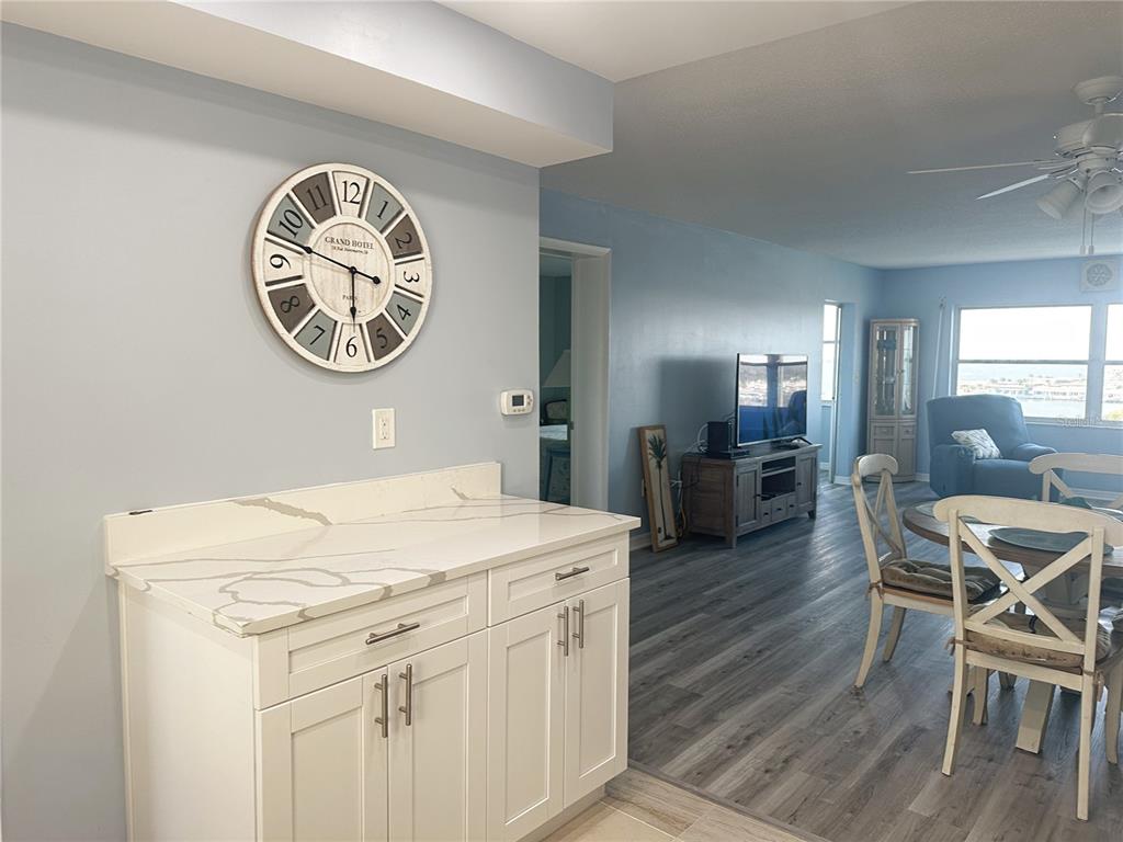 A white cabinet with a marble countertop sits below a large wall clock in a room — 4725 COVE CIRCLE UNIT 804, ST PETERSBURG, FL