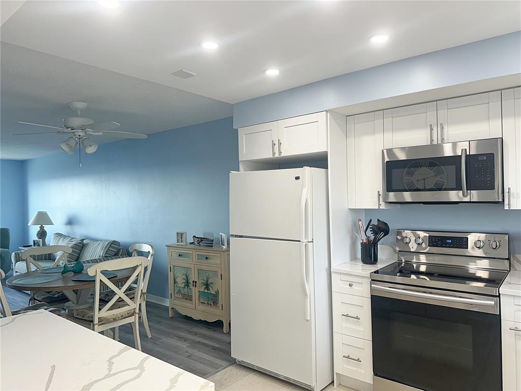A kitchen with white cabinets and stainless steel appliances opens into a blue-walled dining area — 4725 COVE CIRCLE UNIT 804, ST PETERSBURG, FL