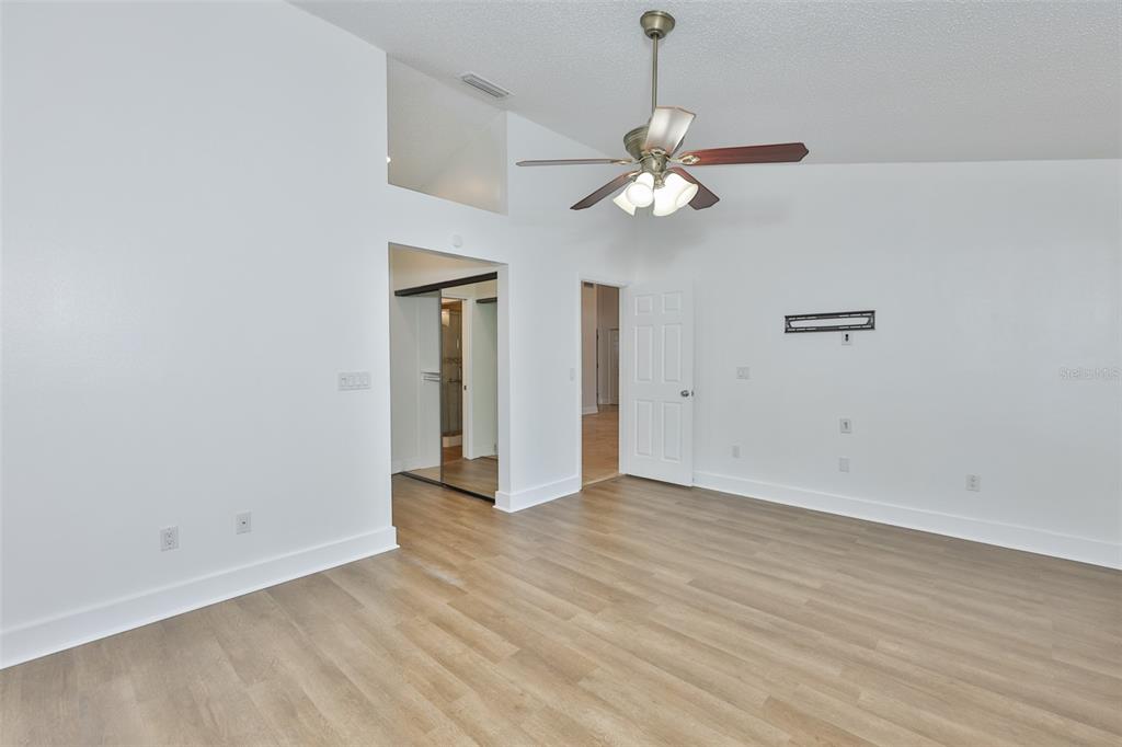 An empty room features light wood-look flooring, white walls, a ceiling fan, and two doorways — 14651 VILLAGE GLEN CIRCLE, TAMPA, FL