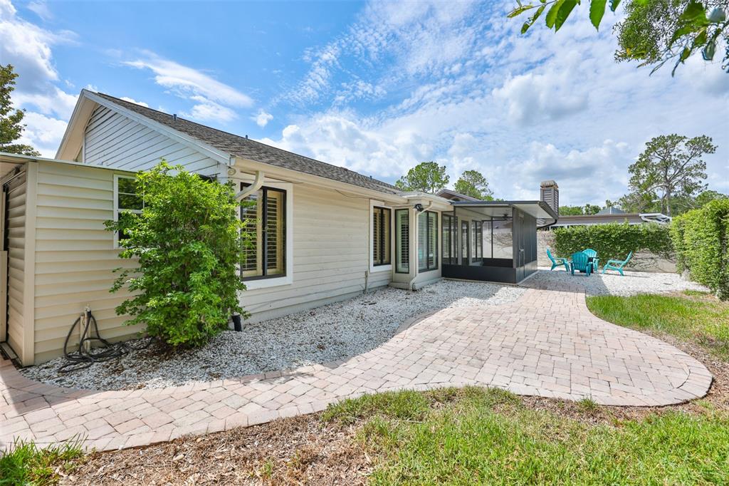 A beige house exterior features a paver patio, a screened-in porch, and white gravel landscaping — 14651 VILLAGE GLEN CIRCLE, TAMPA, FL