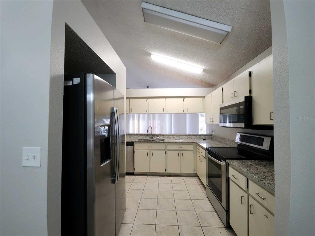 A kitchen features stainless steel appliances, light-colored cabinets, and granite countertops with tile flooring — 8710 TRIPLE OAKS ROAD, TEMPLE TERRACE, FL