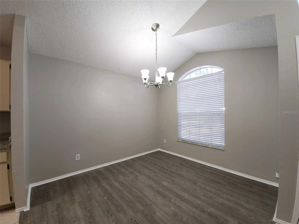 A dining room with grey walls, wood-look flooring, a vaulted ceiling, and a chandelier — 8710 TRIPLE OAKS ROAD, TEMPLE TERRACE, FL