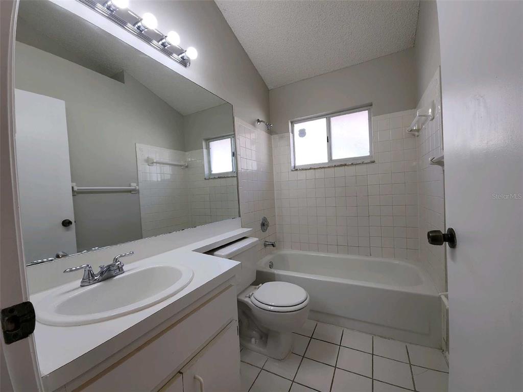 A bathroom features a white vanity, a toilet, and a tiled bathtub shower combination — 8710 TRIPLE OAKS ROAD, TEMPLE TERRACE, FL