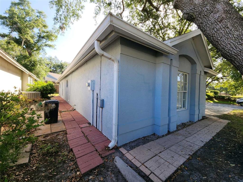 The exterior of a light blue stucco house features a white downspout and brick walkway — 8710 TRIPLE OAKS ROAD, TEMPLE TERRACE, FL