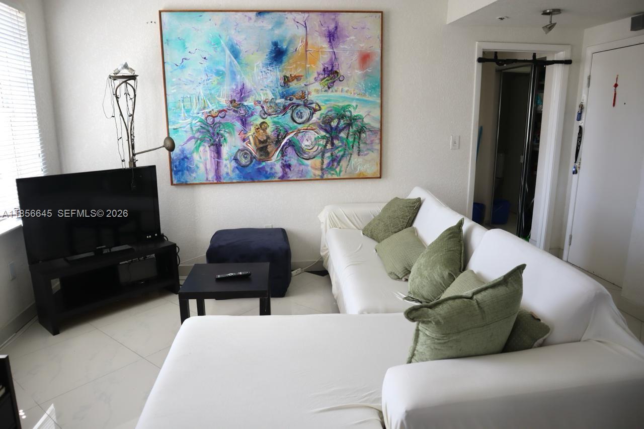 A living room features a white sectional sofa, a television on a stand, and large wall art — 802 Euclid Ave # 305, Miami Beach FL 33139, MIAMI BEACH, FL