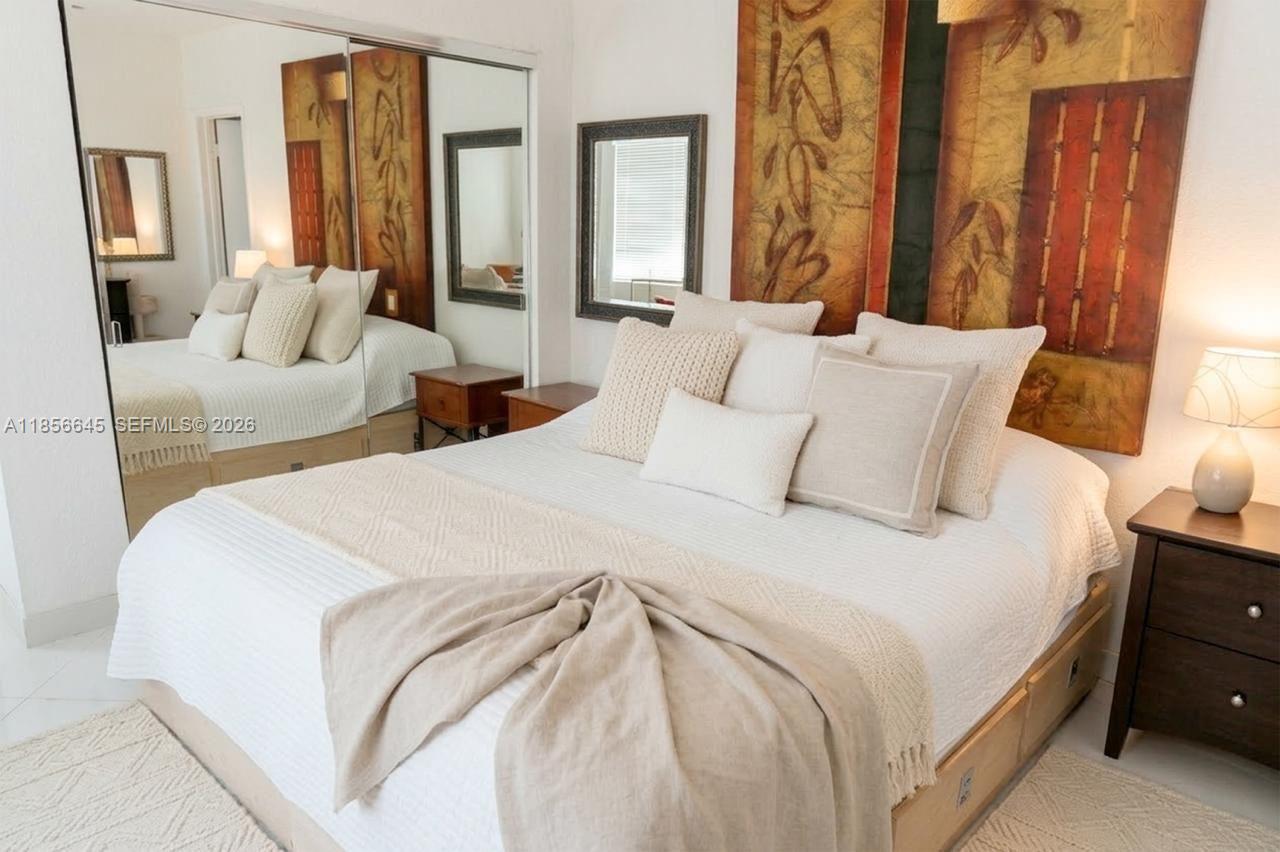 A bedroom features a bed with neutral bedding, a large wall art piece, and mirrored closets — 802 Euclid Ave # 305, Miami Beach FL 33139, MIAMI BEACH, FL