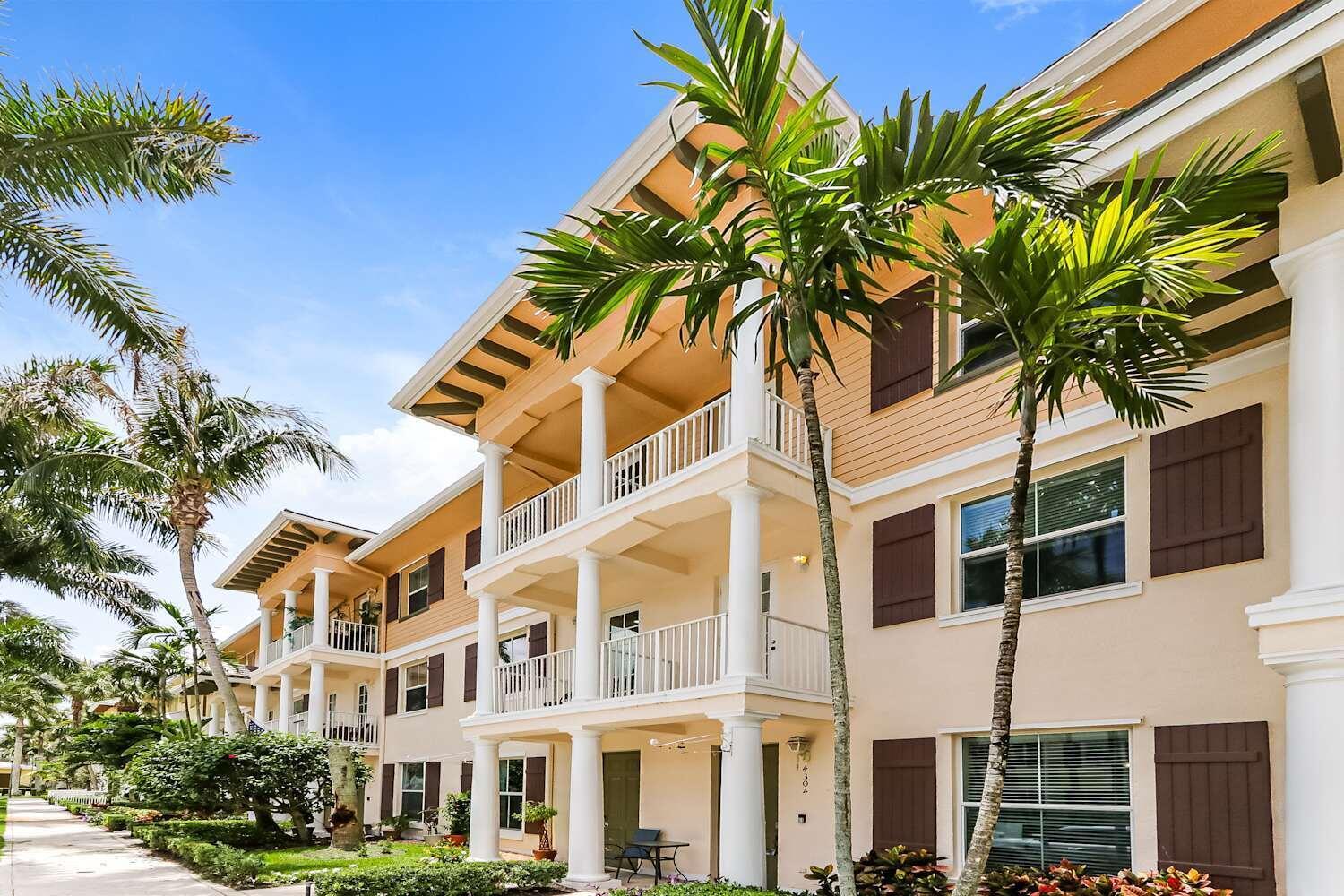 A multi-story apartment building with beige siding, white columns, balconies, and palm trees — JUPITER, FL