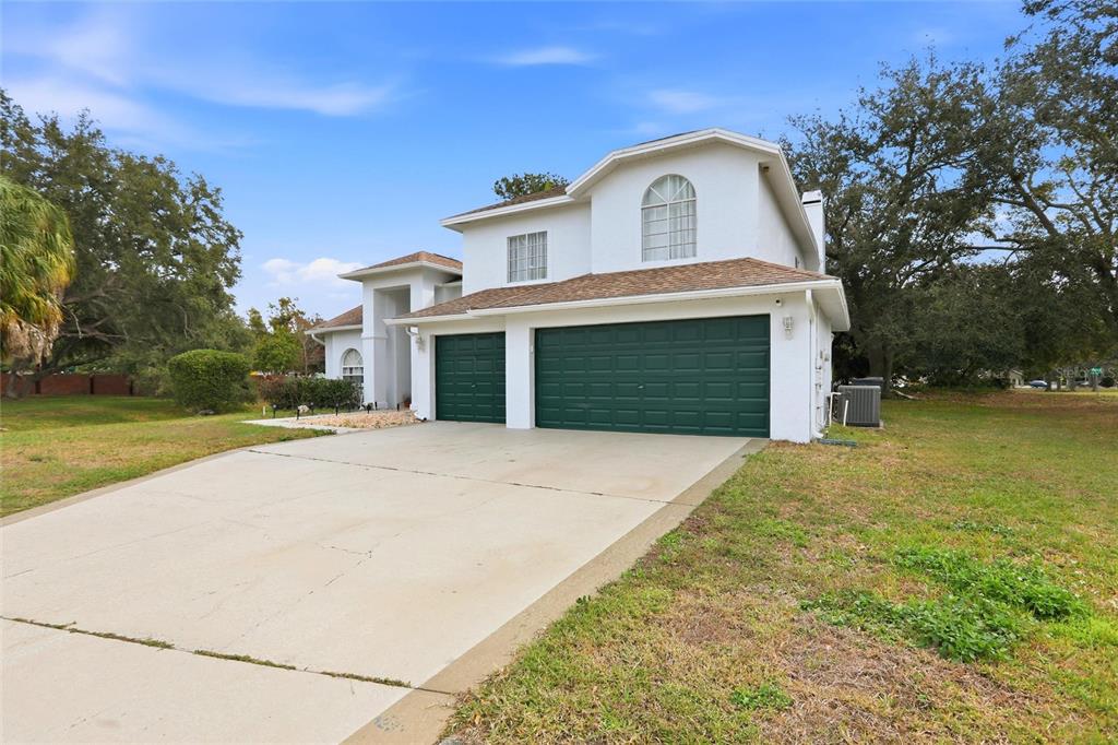 A two-story white house features a three-car garage with dark green doors and a driveway — 10402 ASHLEY OAKS DRIVE, RIVERVIEW, FL