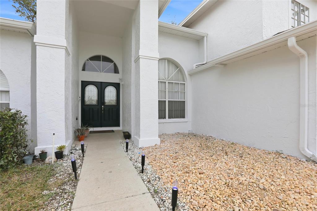 A concrete walkway leads to the dark double front doors of a white stucco house — 10402 ASHLEY OAKS DRIVE, RIVERVIEW, FL