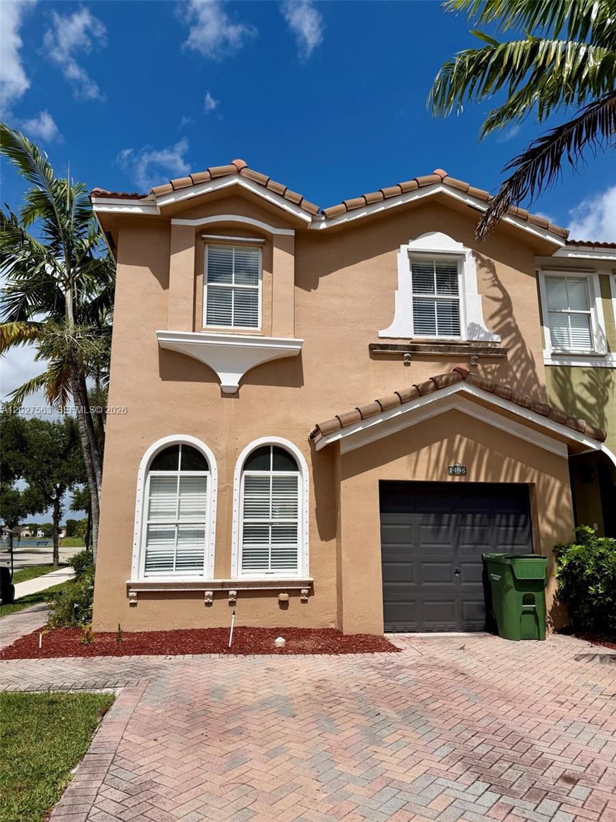 A two-story tan stucco townhouse features a single-car garage and a brick paver driveway — 1498 SE 25th Ave, Homestead FL 33035, HOMESTEAD, FL