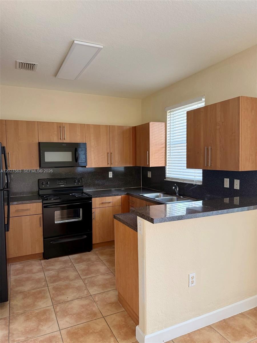 A kitchen features light wood cabinets, black appliances, dark countertops, and tile flooring — 1498 SE 25th Ave, Homestead FL 33035, HOMESTEAD, FL
