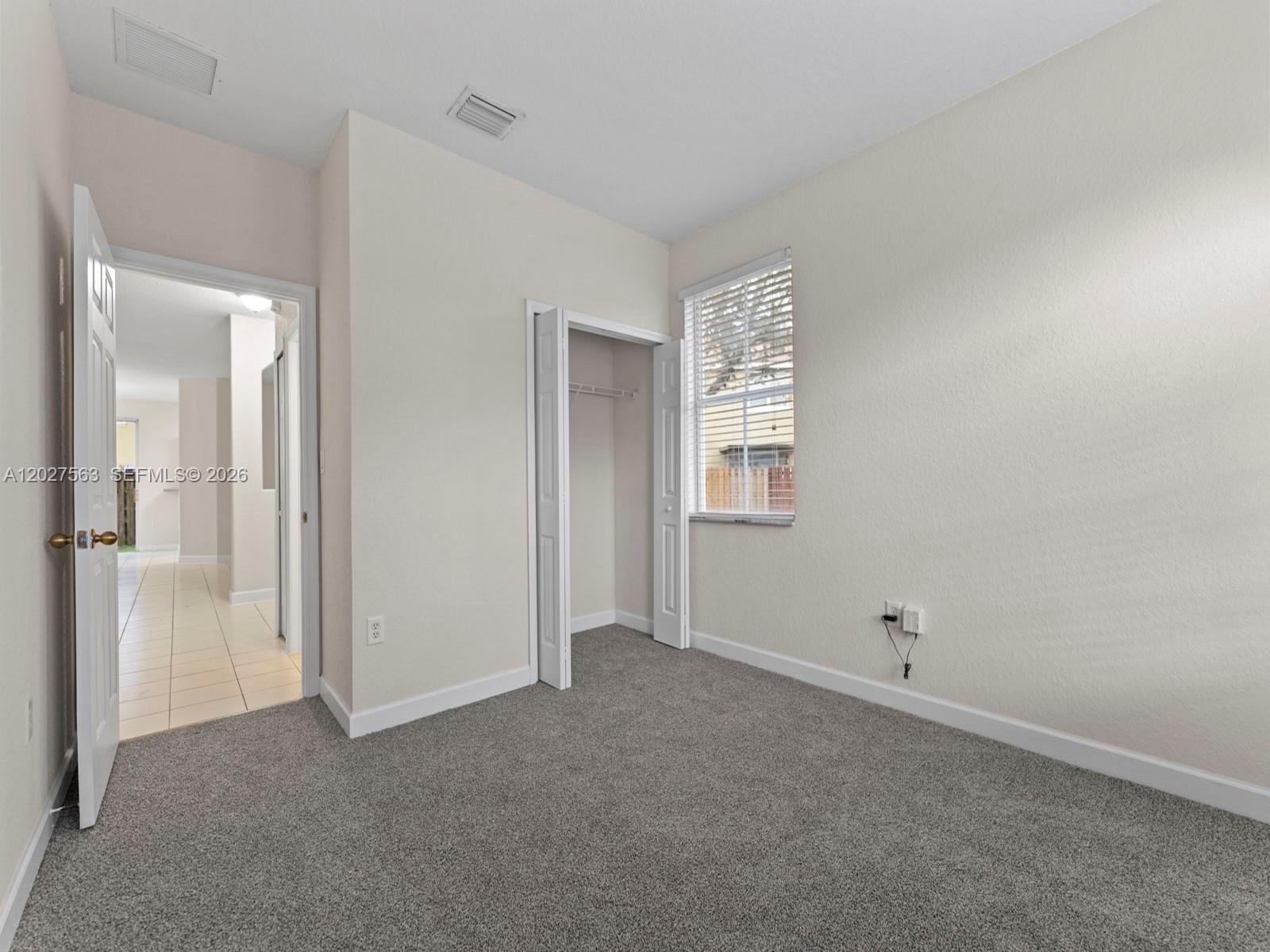 A bedroom with gray carpet, a closet, a window with blinds, and an open doorway — 1498 SE 25th Ave, Homestead FL 33035, HOMESTEAD, FL