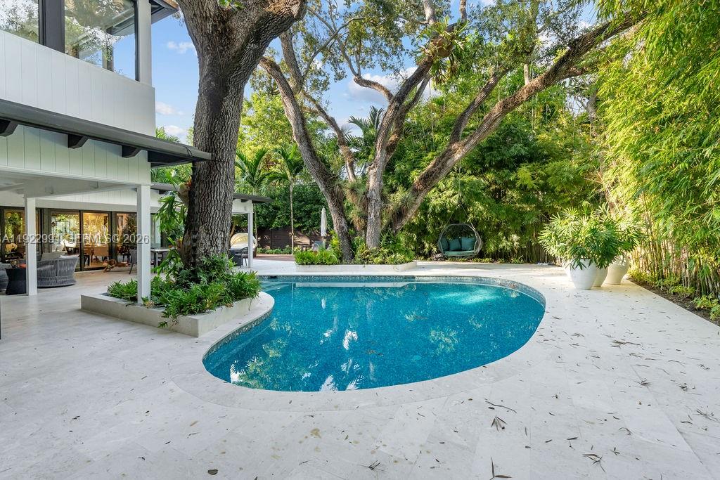 A backyard features a kidney-shaped swimming pool, a large tree, and a modern white house — 4095 Battersea Rd, Miami FL 33133, MIAMI, FL