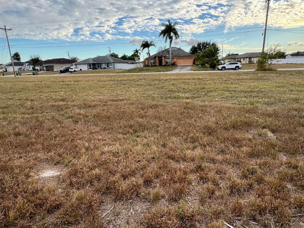 A vacant, grassy lot sits in front of several suburban houses under a cloudy sky — 1845 NE 23RD STREET, CAPE CORAL, FL