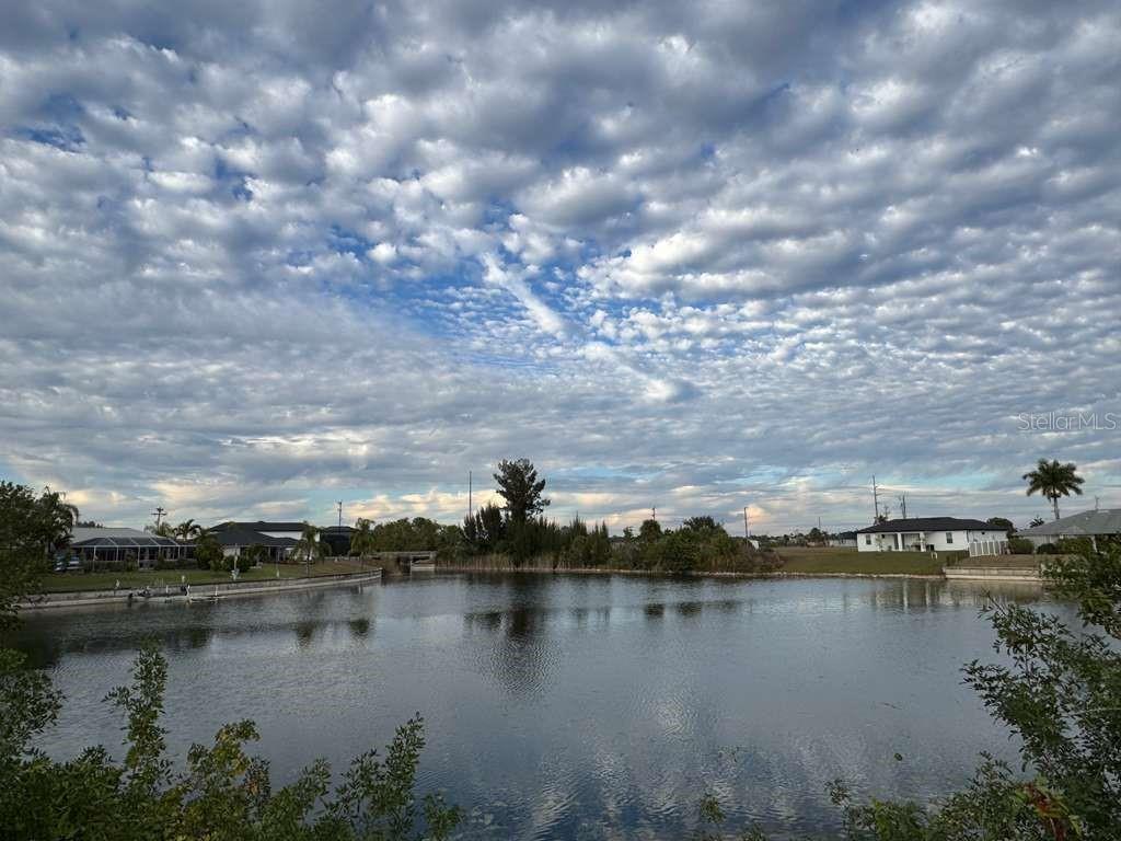 A view of a calm lake surrounded by residential houses under a cloudy blue sky — 1845 NE 23RD STREET, CAPE CORAL, FL