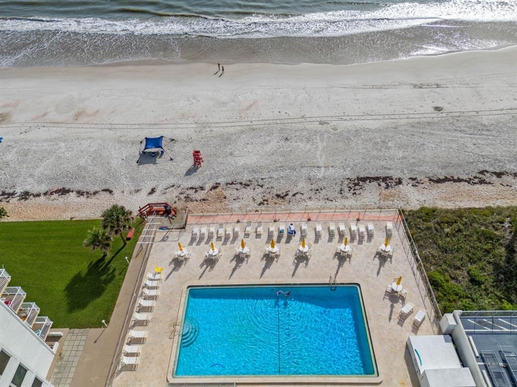 An aerial view shows a rectangular swimming pool with lounge chairs and tables beside a beach — 5201 S ATLANTIC AVENUE UNIT 703A, NEW SMYRNA BEACH, FL