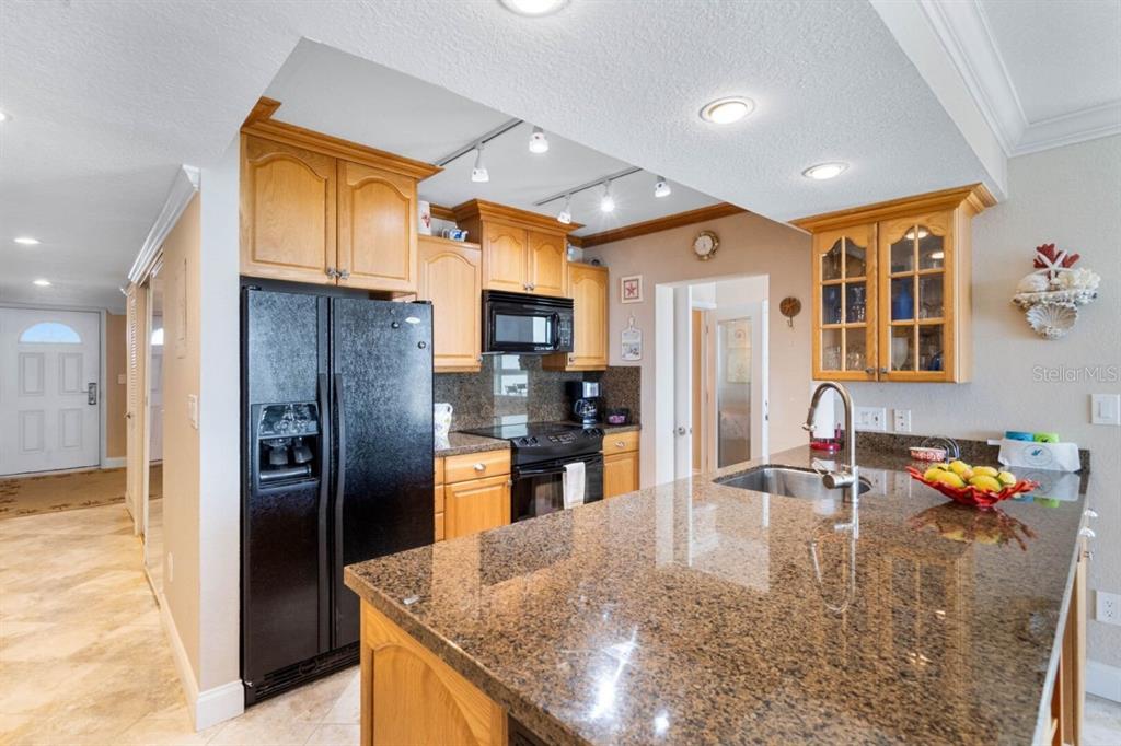 A kitchen features oak cabinets, black appliances, and a granite-topped island with a sink — 5201 S ATLANTIC AVENUE UNIT 703A, NEW SMYRNA BEACH, FL