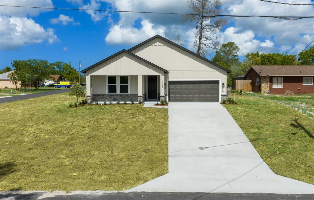 A modern single-story house with a beige vertical-siding facade, stone base, and a concrete driveway — 10153 LYNNHAVEN ROAD, SPRING HILL, FL