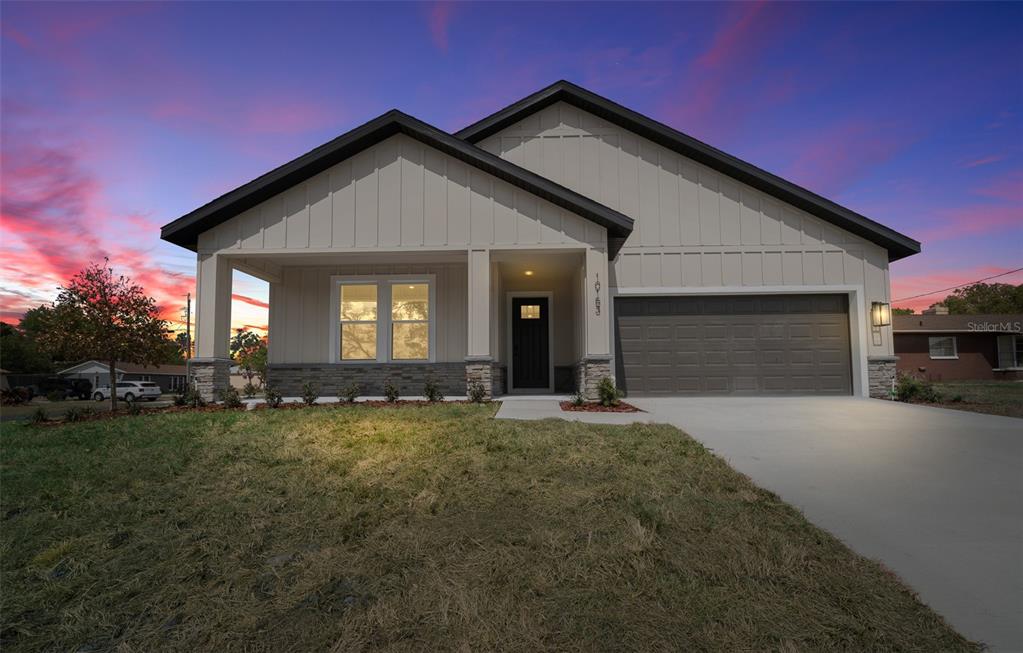 A single-story house with a gray garage, stone accents, and vertical siding at sunset — 10153 LYNNHAVEN ROAD, SPRING HILL, FL