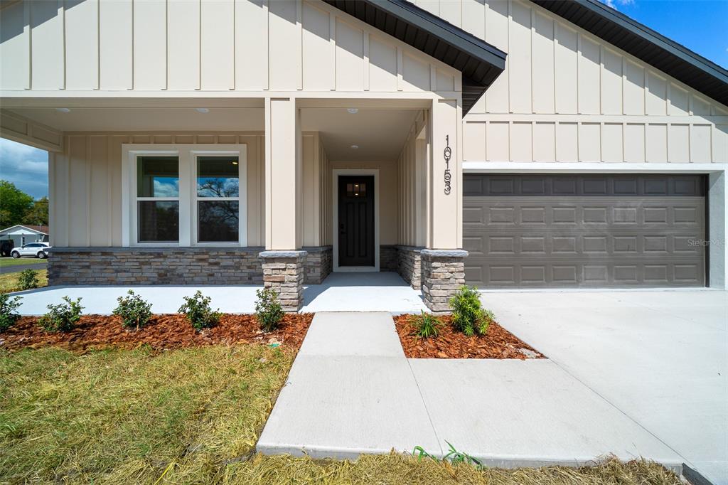 The exterior of a house features beige vertical siding, stone accents, a dark door, and a garage — 10153 LYNNHAVEN ROAD, SPRING HILL, FL