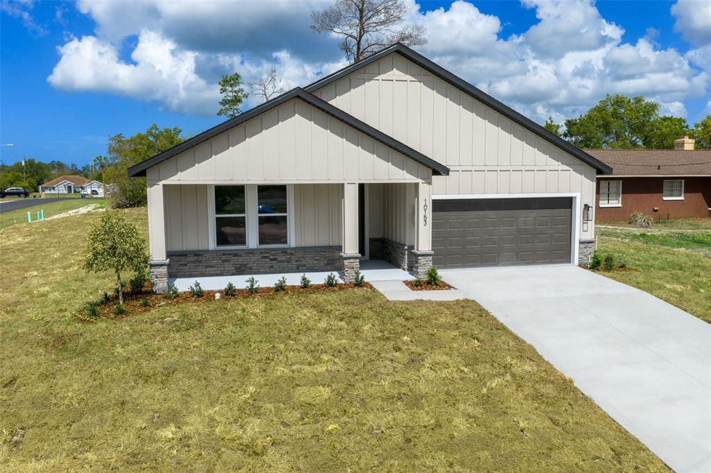 A single-story house with light-colored vertical siding, a stone base, and a two-car garage — 10153 LYNNHAVEN ROAD, SPRING HILL, FL