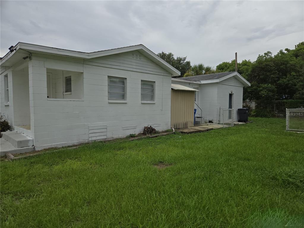 The exterior of a white concrete block house with a grassy yard and metal shed — 1402 MALUHIA DRIVE, TAMPA, FL