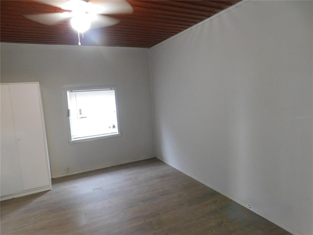 A bedroom with light-colored walls, wood-look flooring, a white wardrobe, and a wood-paneled ceiling — 1402 MALUHIA DRIVE, TAMPA, FL