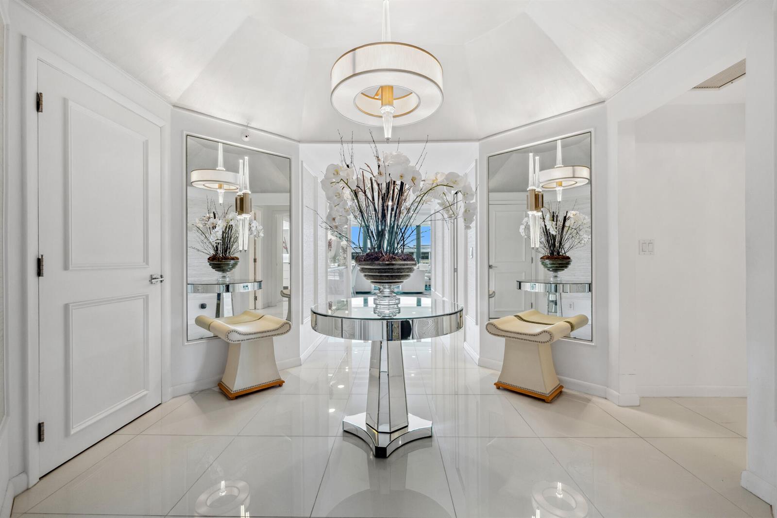 A bright, symmetrical foyer features white tile floors, mirrored console tables, and a central pedestal table — 2100 S Ocean Boulevard # 607n, Palm Beach FL 33480, PALM BEACH, FL