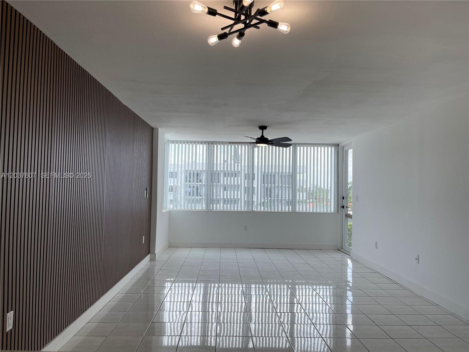 An empty room features white tile floors, a wood-slat accent wall, and a ceiling fan — 8233 Harding Ave # 408, Miami Beach FL 33141, MIAMI BEACH, FL