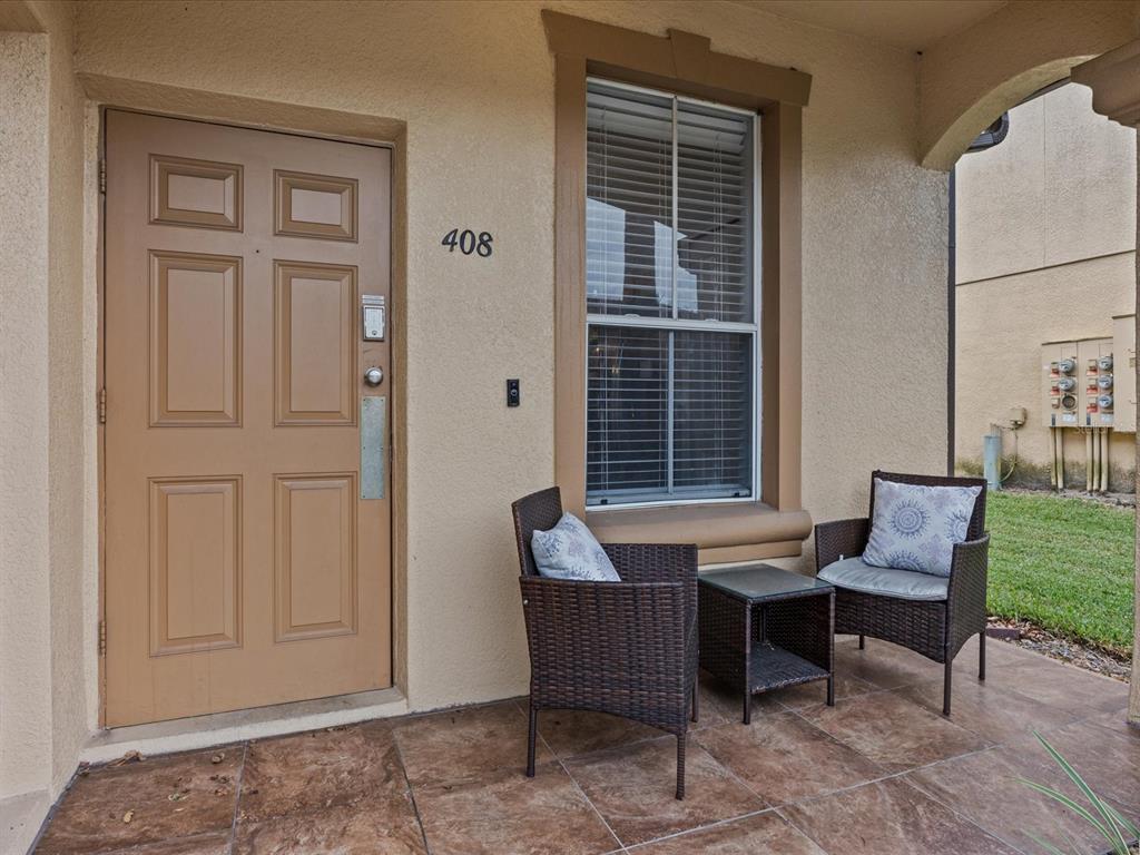 A tan front door and a window with two wicker chairs on a tiled porch — 408 MIRAMAR AVENUE, DAVENPORT, FL
