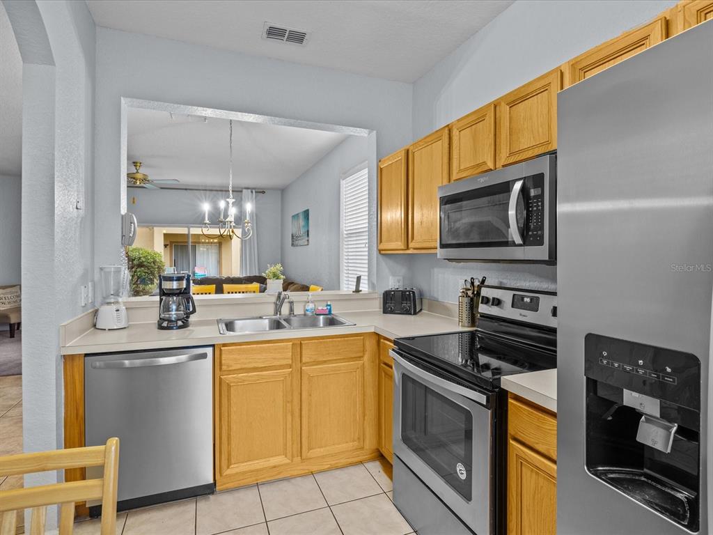 A kitchen features light wood cabinets, stainless steel appliances, and a pass-through window to the living area — 408 MIRAMAR AVENUE, DAVENPORT, FL