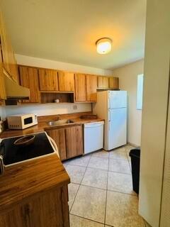 A kitchen features wood cabinets, a white refrigerator, a black stovetop, and tiled flooring — 505 Gardens Drive # 204, Pompano Beach FL 33069, POMPANO BEACH, FL