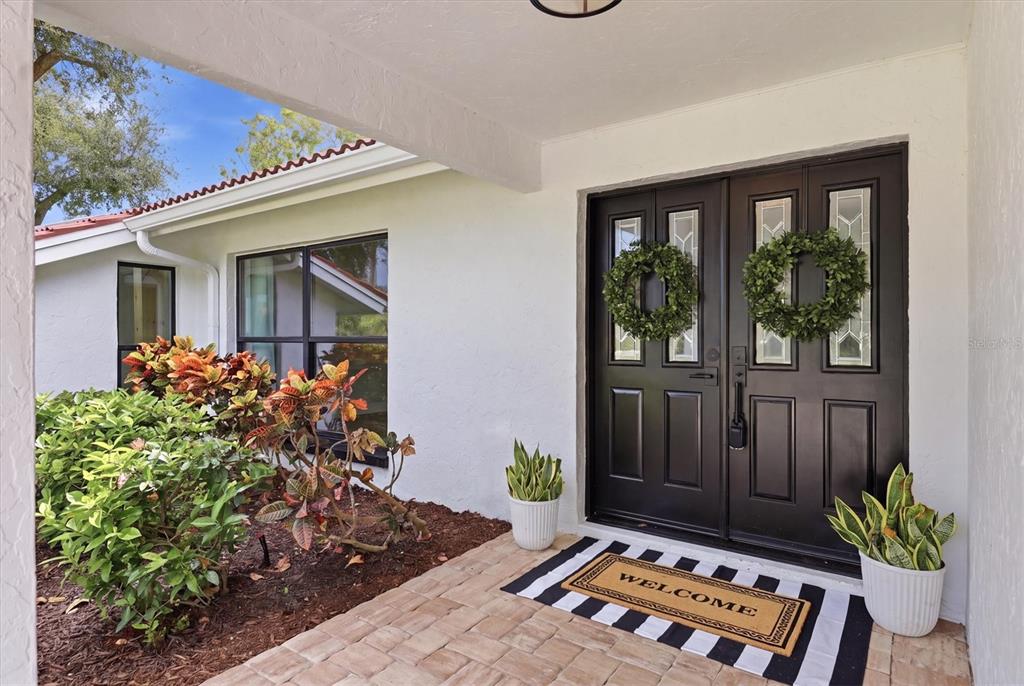 A front porch features a black double door with wreaths and a striped welcome mat — 8822 MISTY CREEK DRIVE, SARASOTA, FL