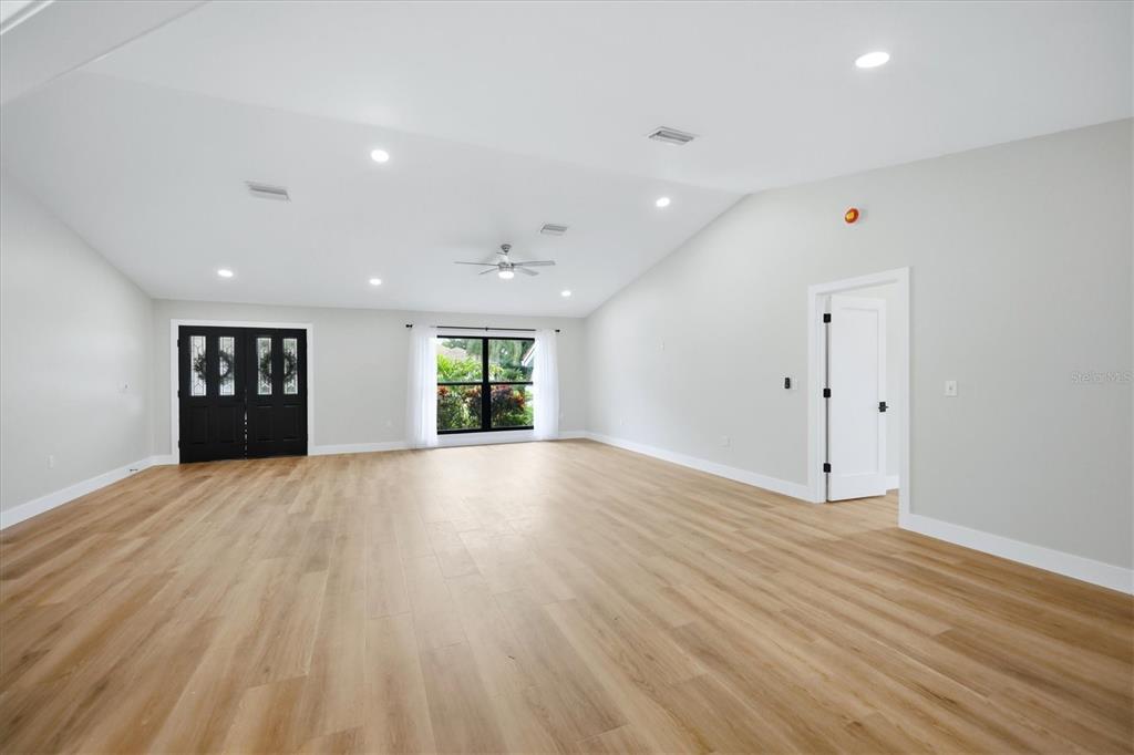 A spacious, empty room with light wood-look flooring, white walls, and a vaulted ceiling — 8822 MISTY CREEK DRIVE, SARASOTA, FL