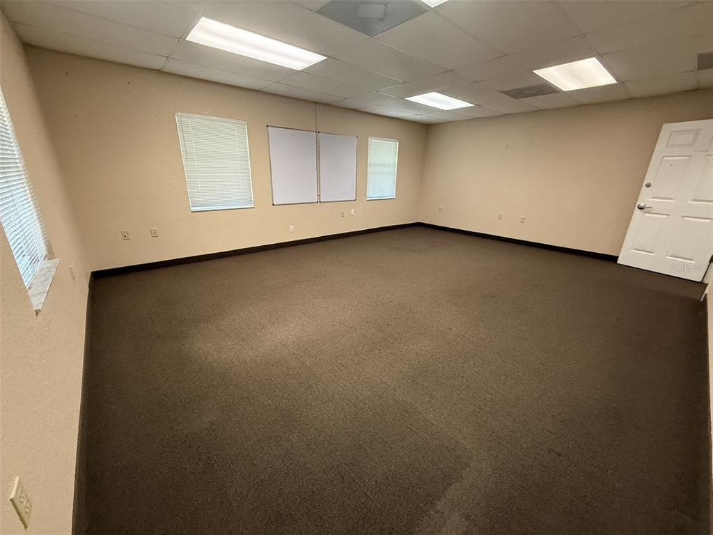 An empty office room features beige walls, dark carpeting, drop ceiling lights, and a white door — 2609 SW 33RD STREET UNIT 101-4, OCALA, FL