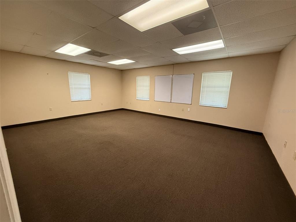 An empty office room features beige walls, dark carpeting, drop ceiling lights, and whiteboards — 2609 SW 33RD STREET UNIT 101-4, OCALA, FL